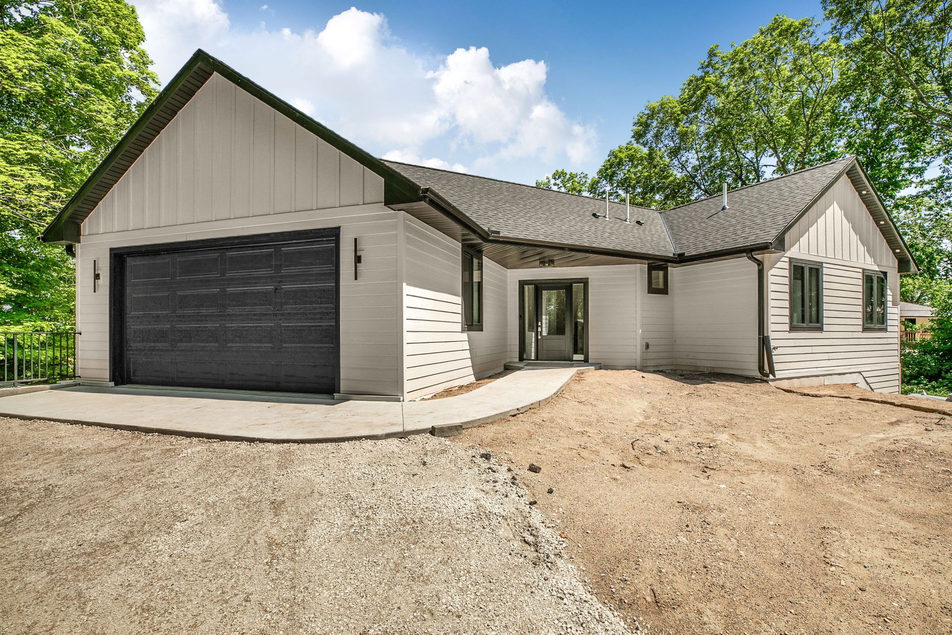 Modern white house with black garage door and gravel driveway under construction