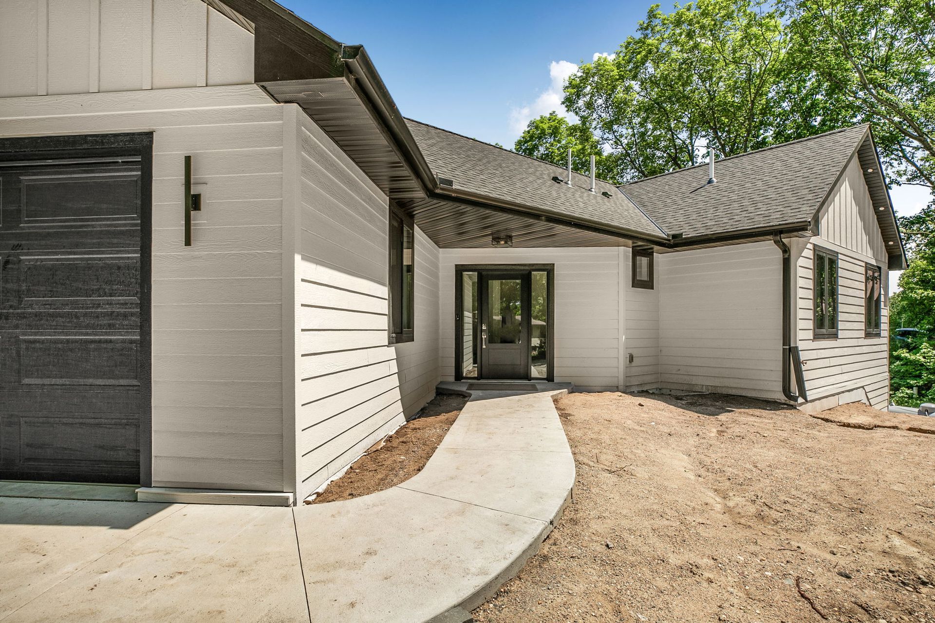 Modern white house exterior with curved concrete walkway and dirt yard