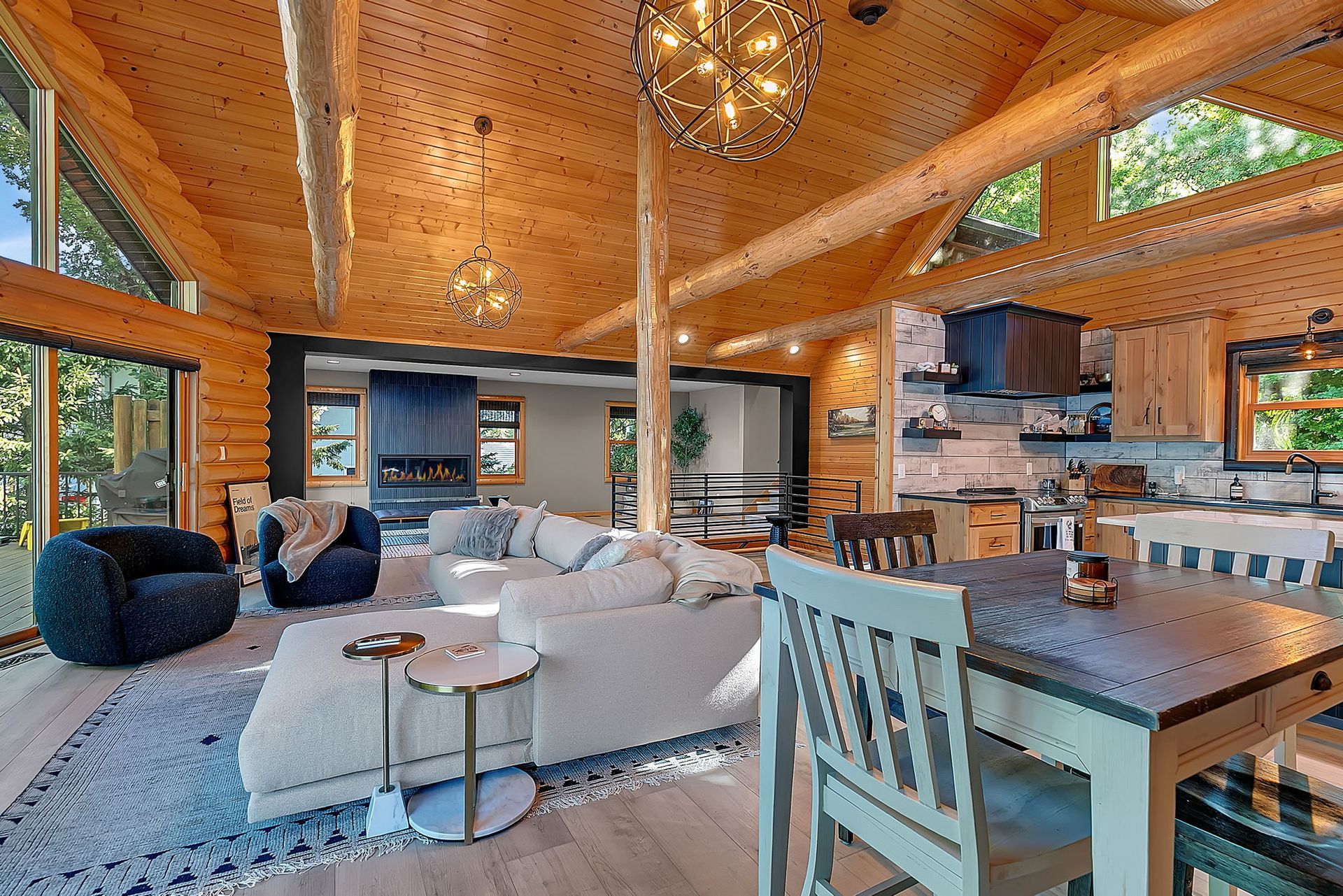 Cozy wooden cabin living room with vaulted ceiling, sofa, chairs, and large windows