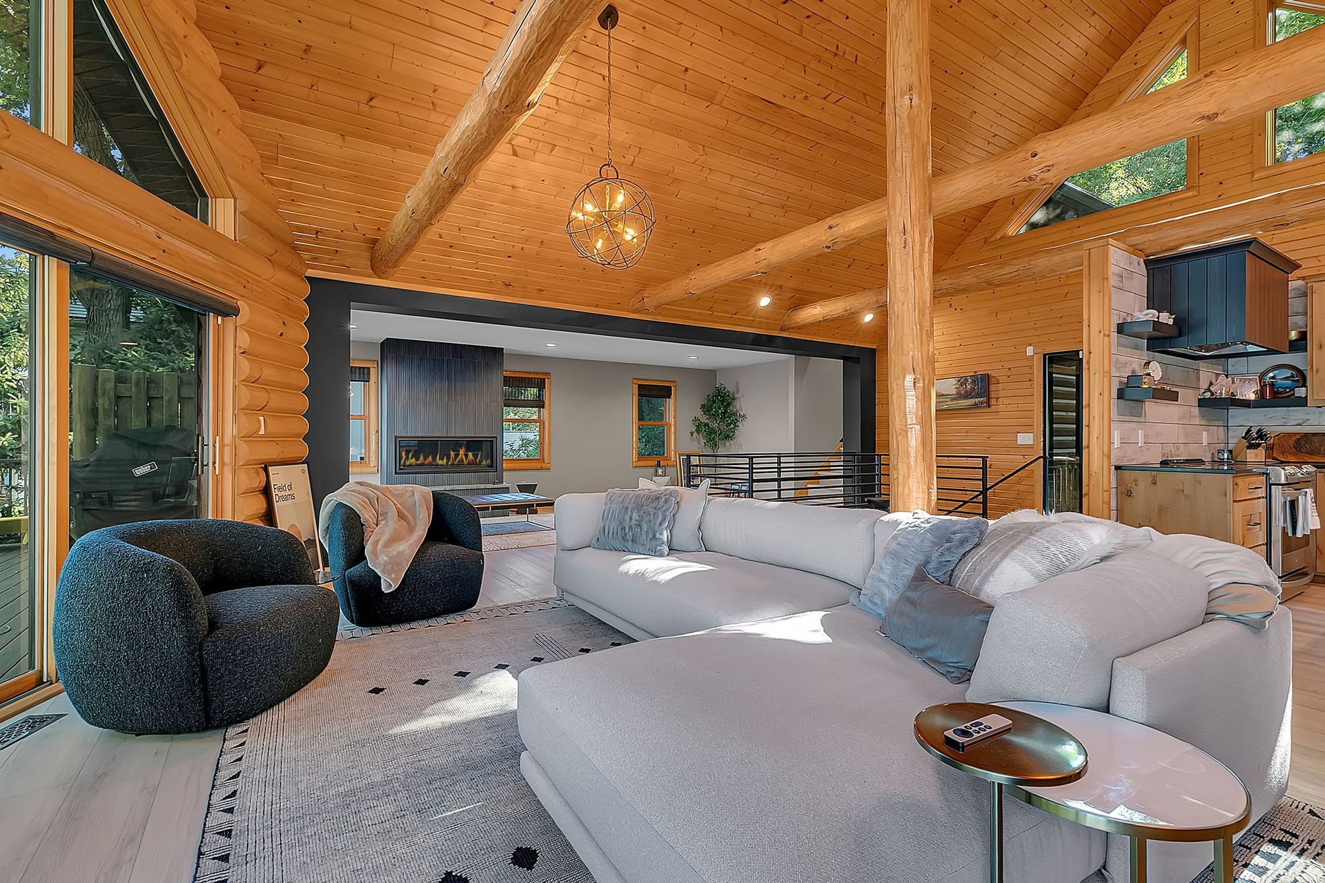Modern timber living room with large gray sectional, black chair, and wall of windows overlooking trees
