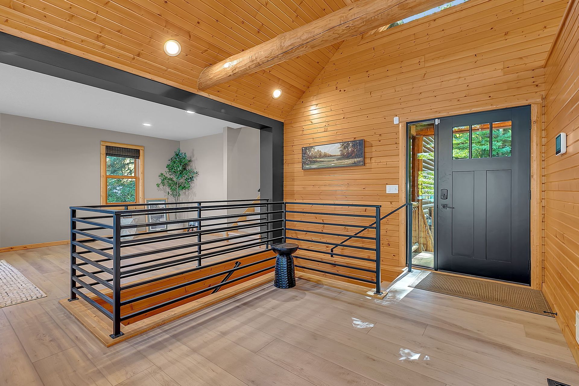 Modern loft landing with wood ceiling, black railings, skylight, and a dark door to the right.