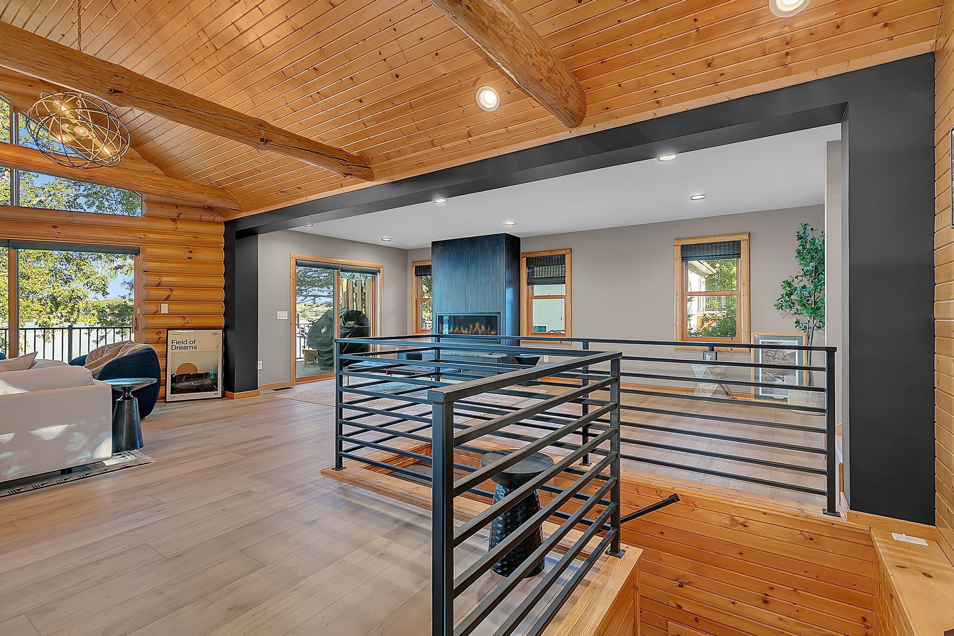 Modern open-concept living room with wood ceiling, stairs, and large windows