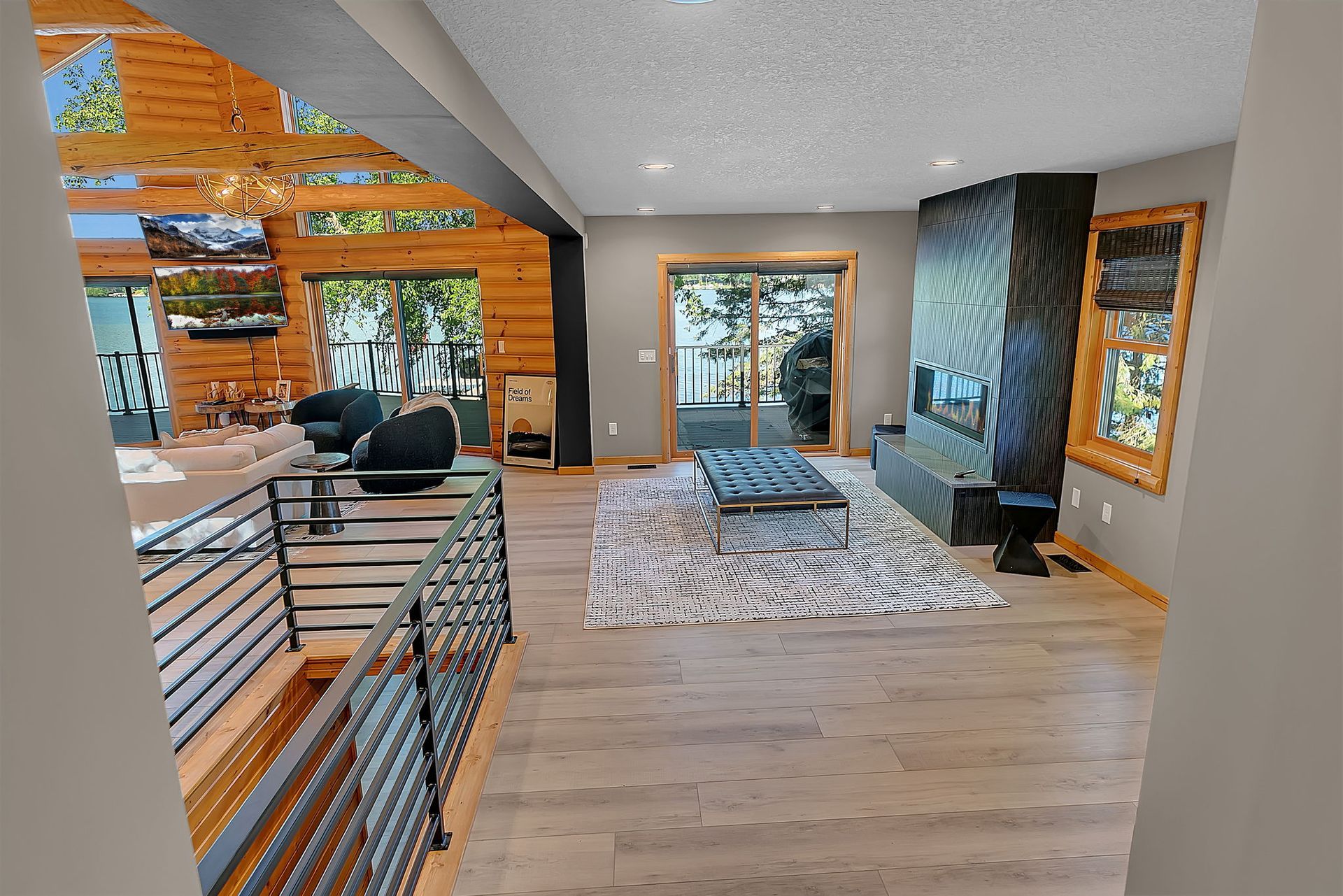 Modern living room with wood floors, patterned rug, black sofa, and large windows overlooking trees