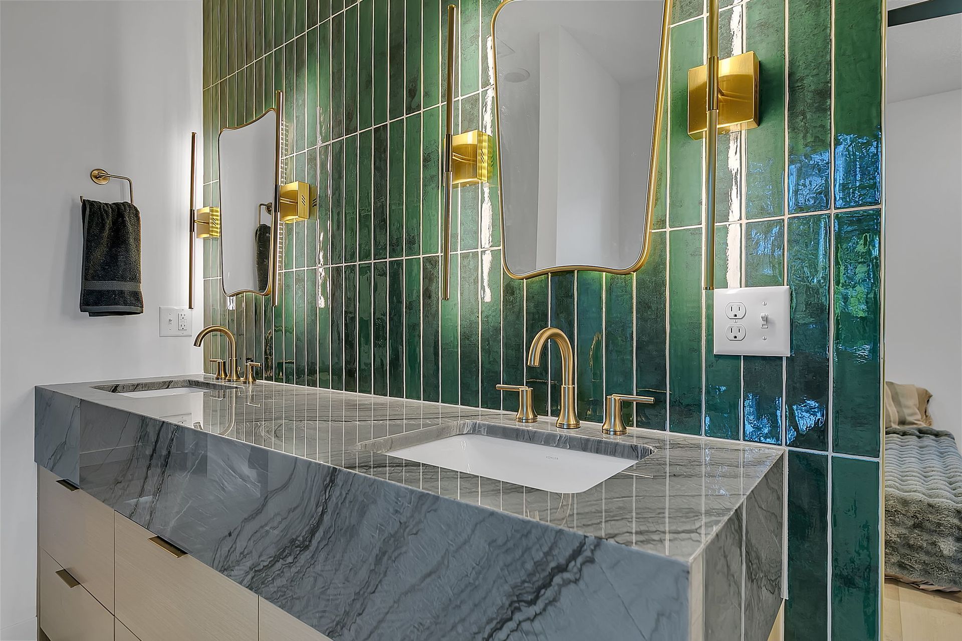 Modern bathroom vanity with gray marble counter, green glass tile wall, and gold faucets