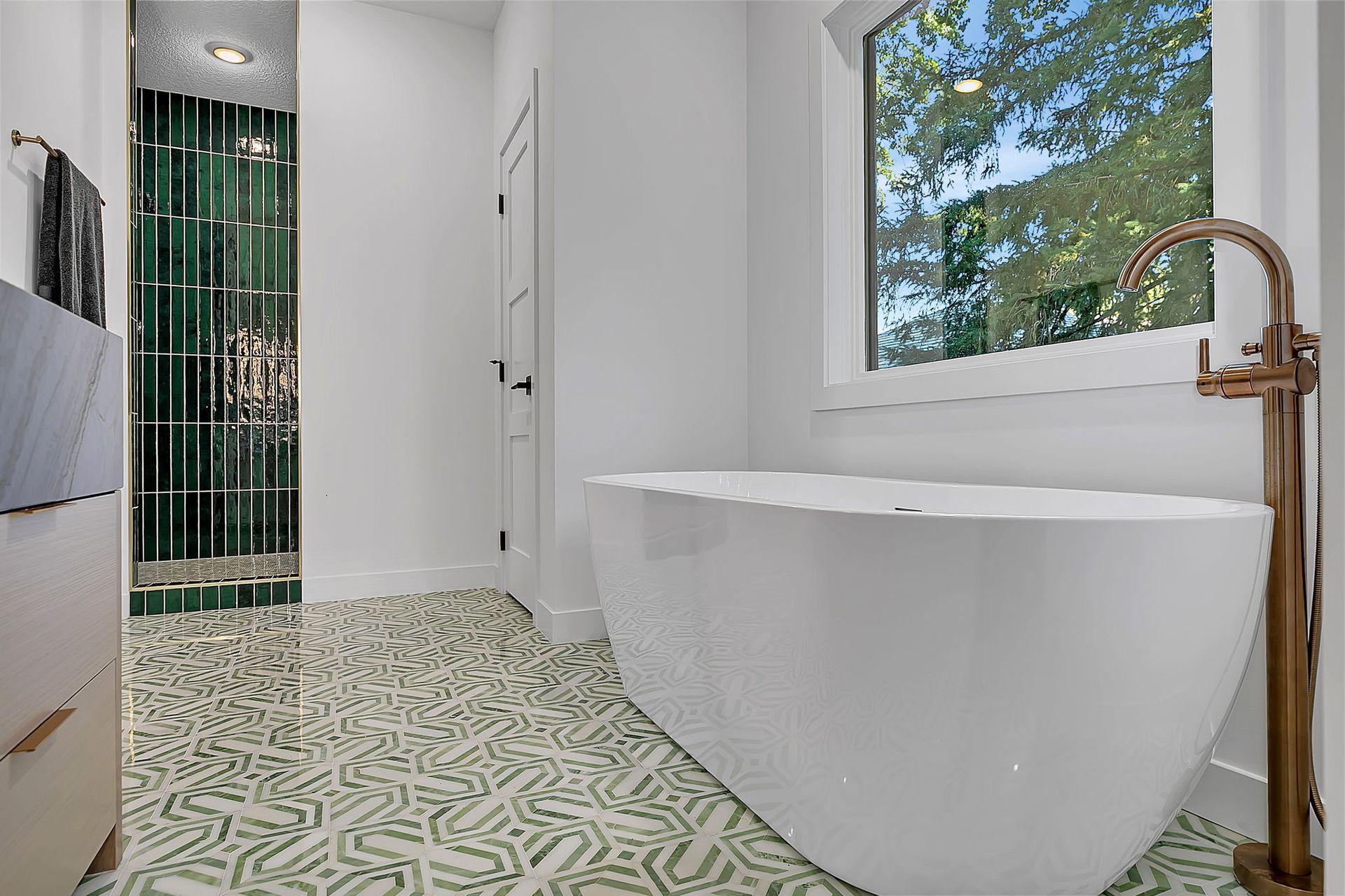 Modern bathroom with white tub, green patterned floor, and glass shower door