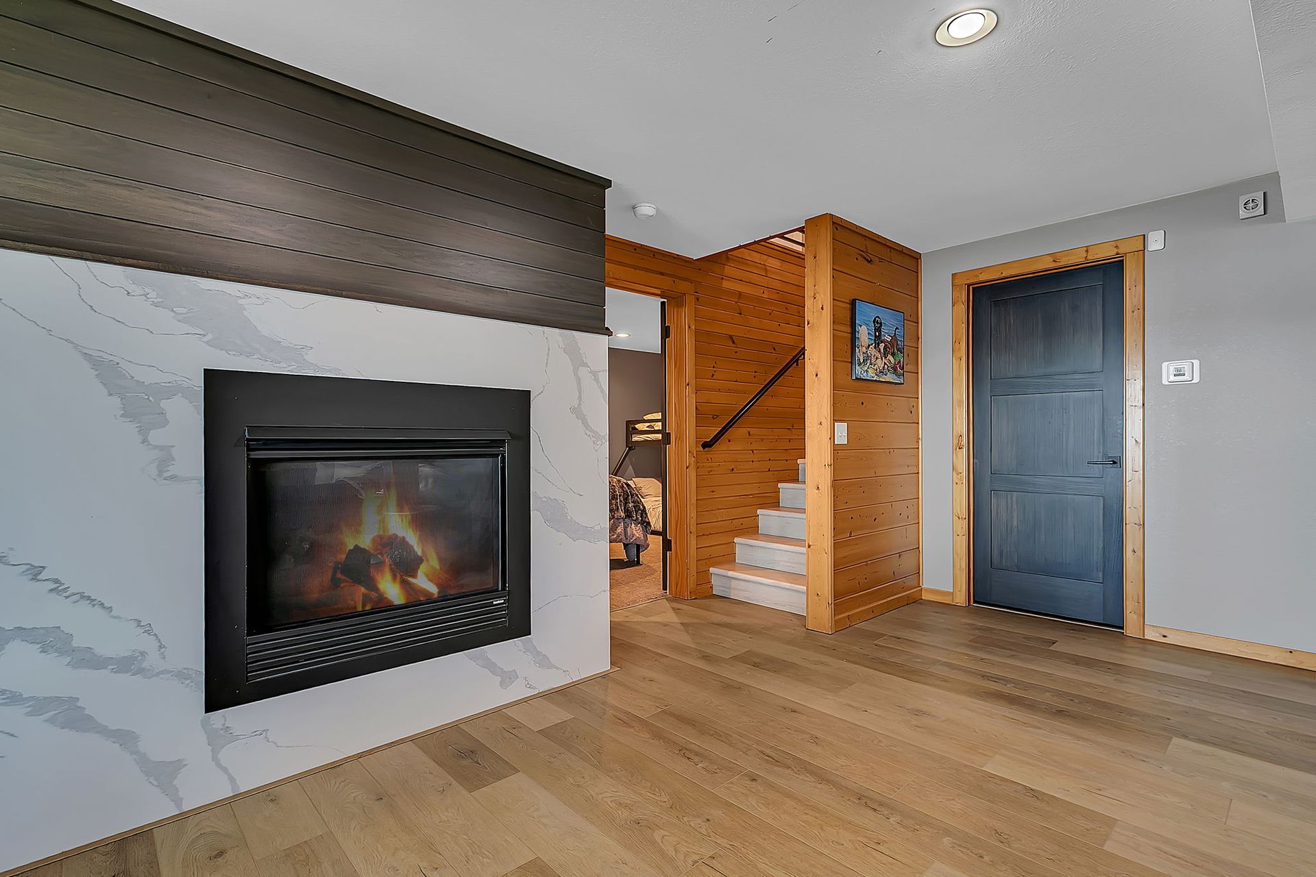 Modern living room with a wall fireplace, wood floors, staircase, and gray and blue doors