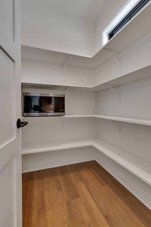 An empty pantry with wooden floors and white shelves.