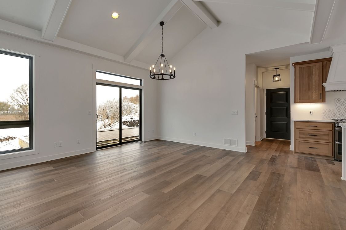An empty living room with hardwood floors and a chandelier hanging from the ceiling.