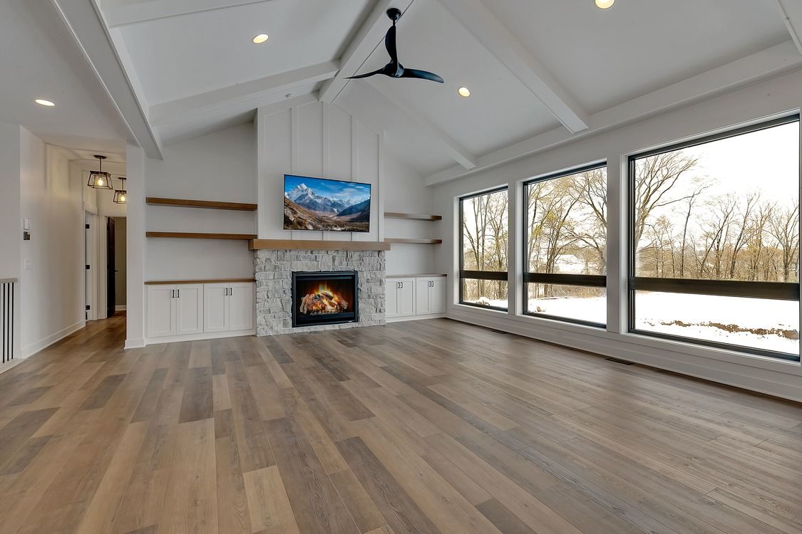 An empty living room with hardwood floors , a fireplace , and lots of windows.