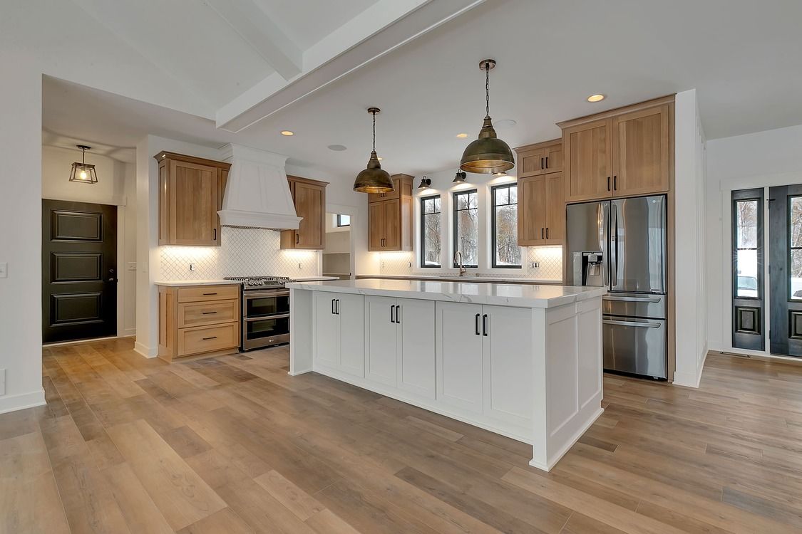 A kitchen with white cabinets , wooden floors , stainless steel appliances and a large island.