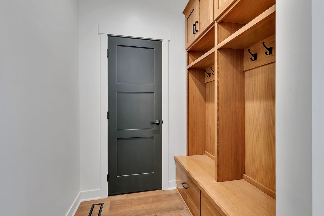 A hallway with a black door and wooden cabinets.