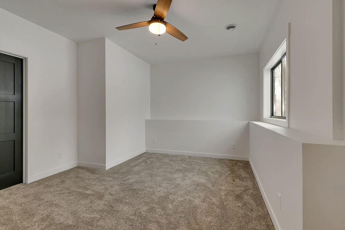 An empty room with a ceiling fan and a window.