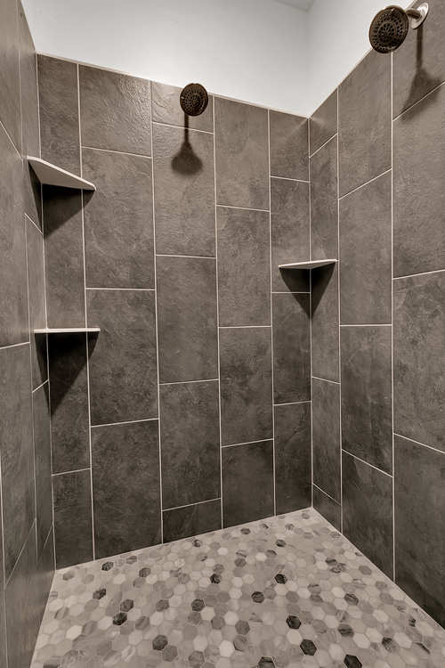 A walk in shower with two shower heads and shelves.