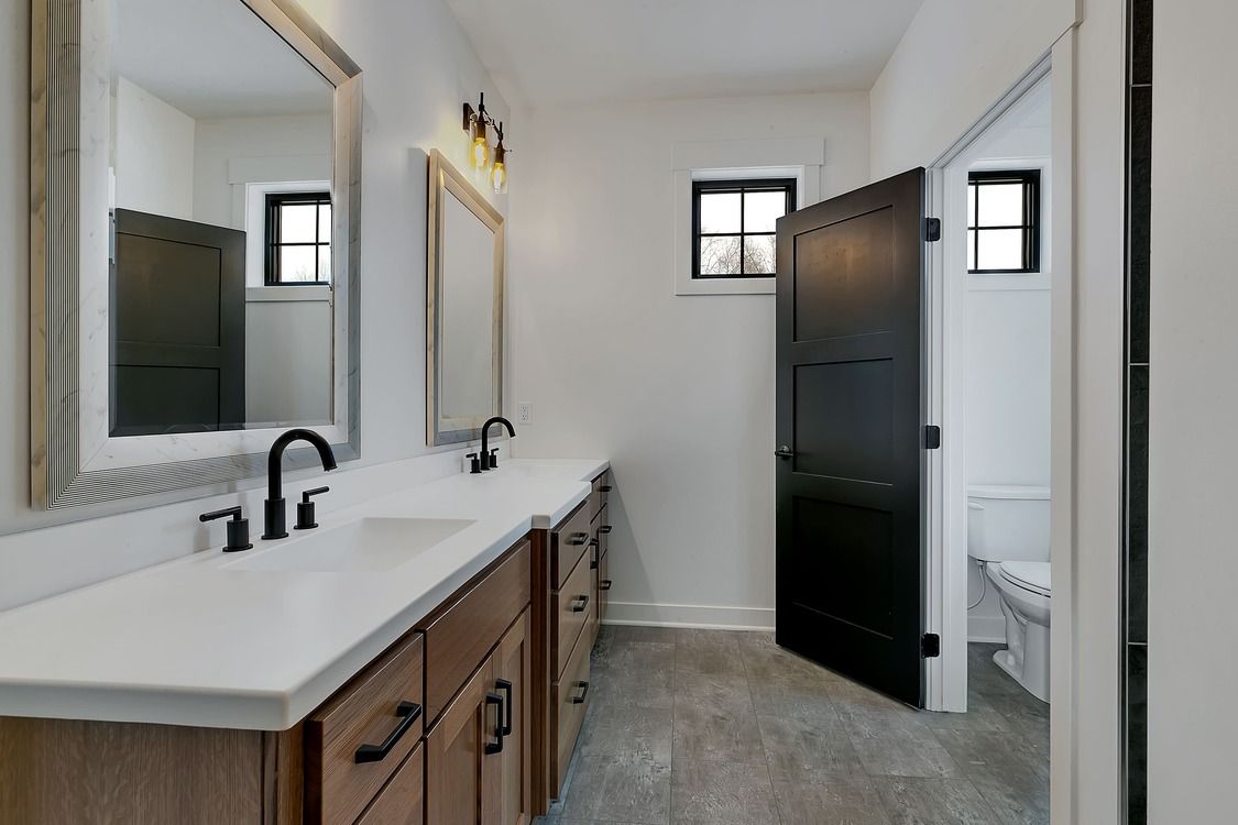 A bathroom with two sinks , two mirrors and a toilet.