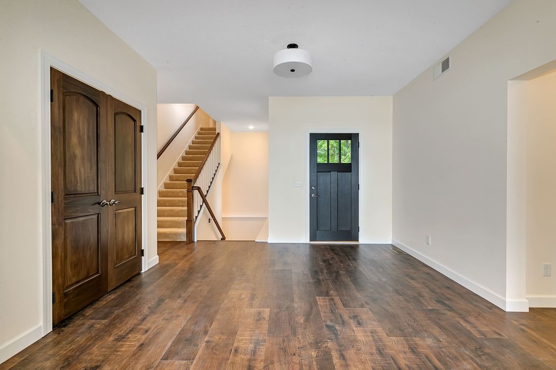 An empty room with hardwood floors and a staircase in the background.