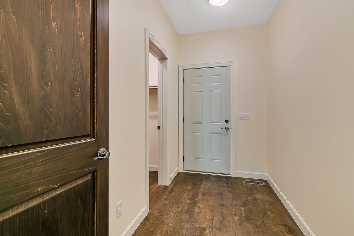 A hallway with hardwood floors and a wooden door in a house.