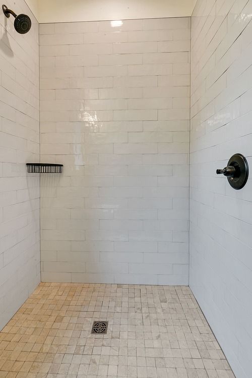 A walk in shower with white tiles and a black shower head.