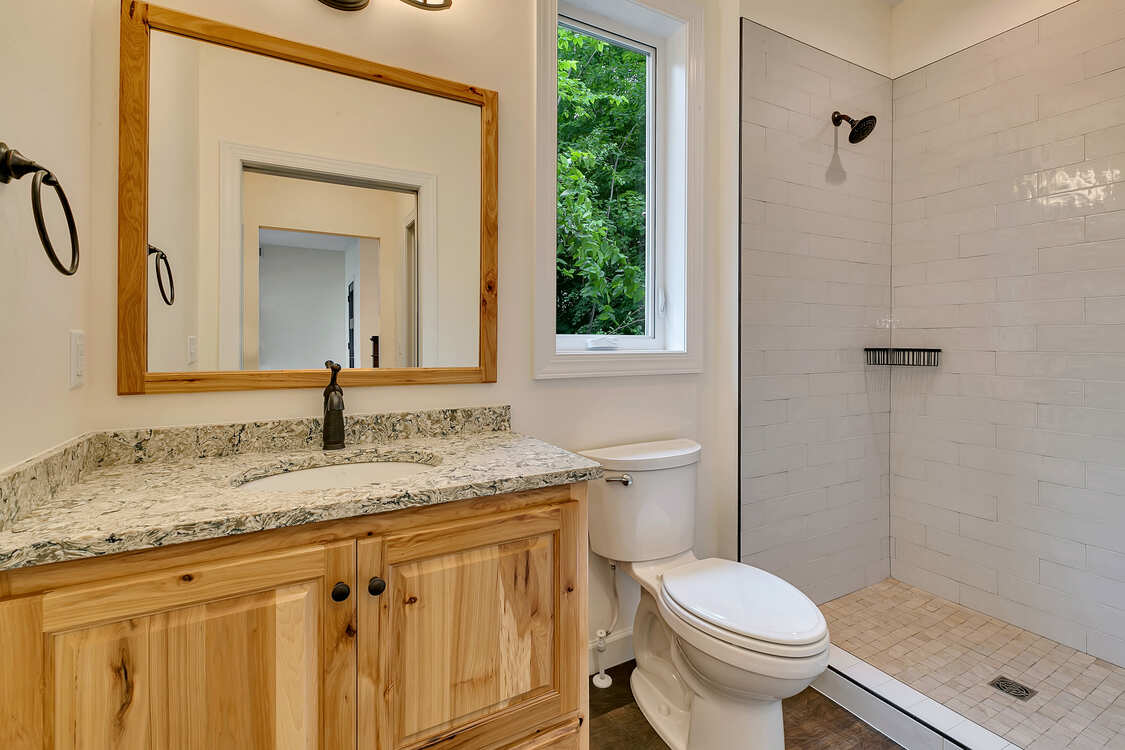 A bathroom with a toilet , sink , mirror and walk in shower.