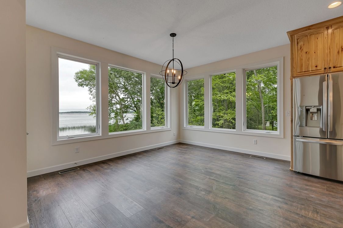 An empty living room with a lot of windows and a refrigerator.