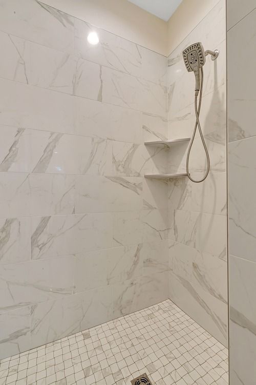 A walk in shower with marble tiles and a shower head.