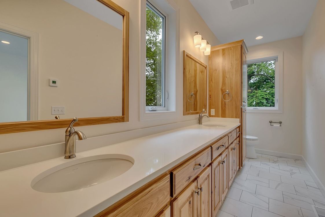 A bathroom with two sinks , two mirrors and a window.