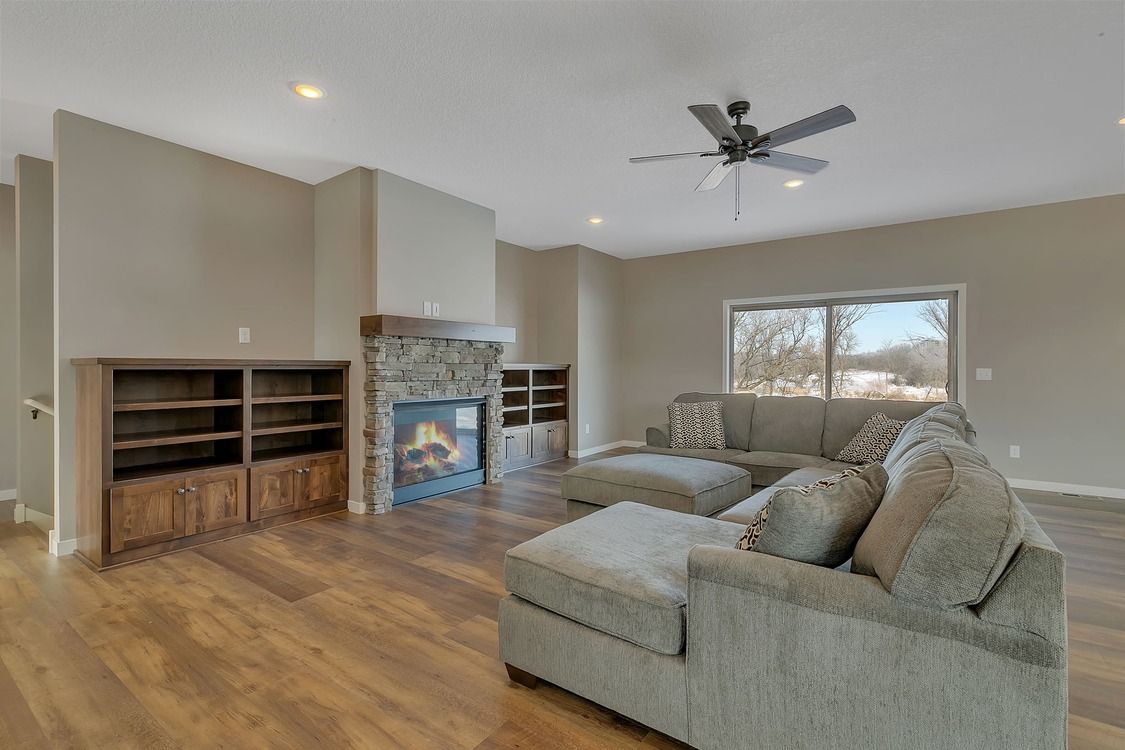 A living room with a couch , ottoman , fireplace and ceiling fan.