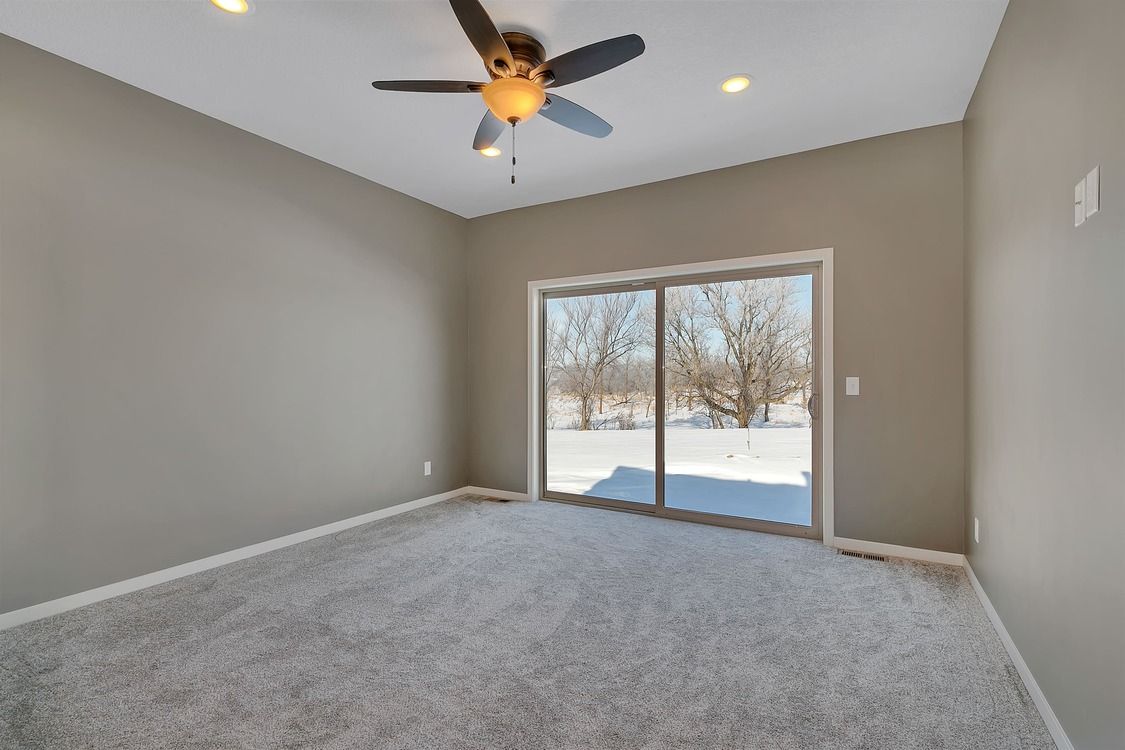 An empty room with a ceiling fan and a sliding glass door.