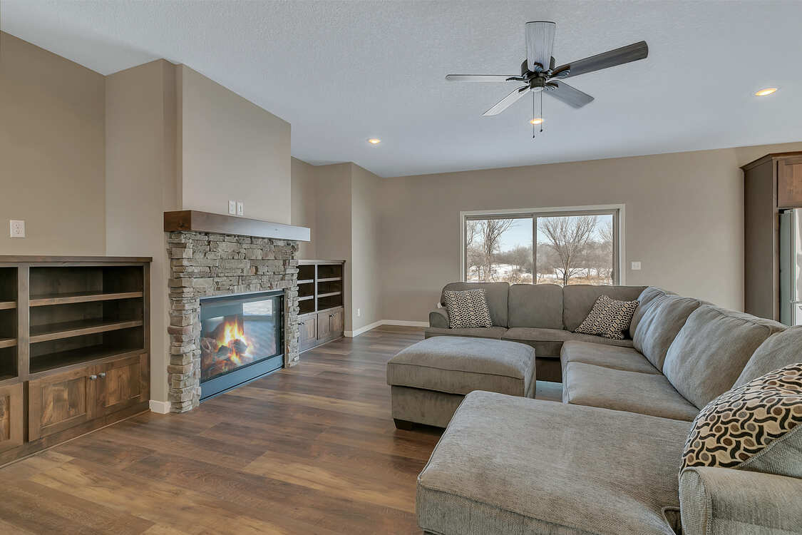 A living room with a couch , ottoman , fireplace and ceiling fan.