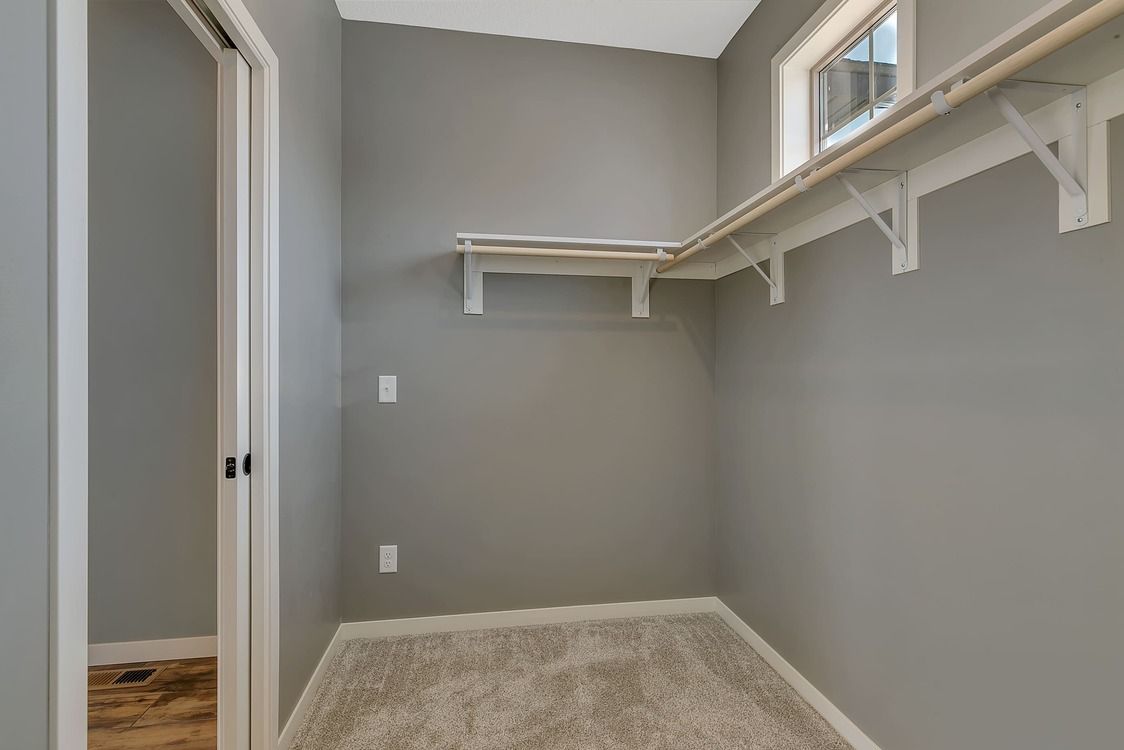 An empty walk in closet with gray walls and white shelves.