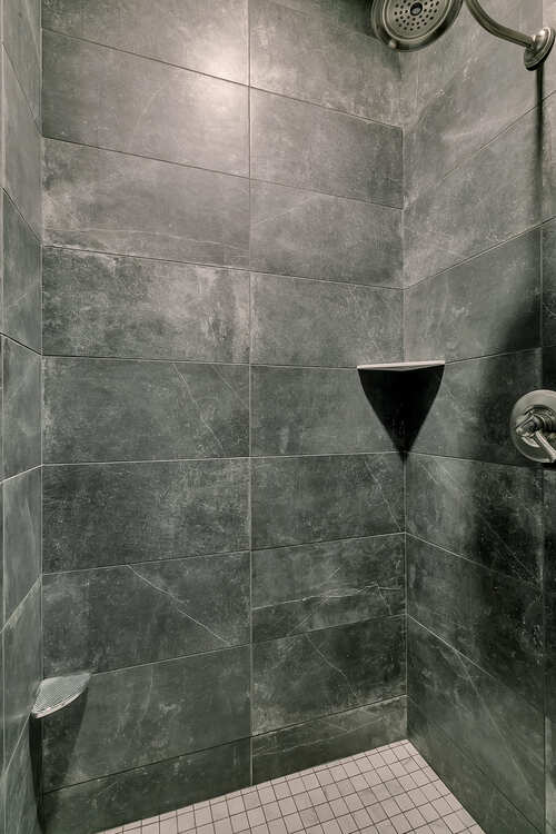 A shower with a shower head and a shelf in it.