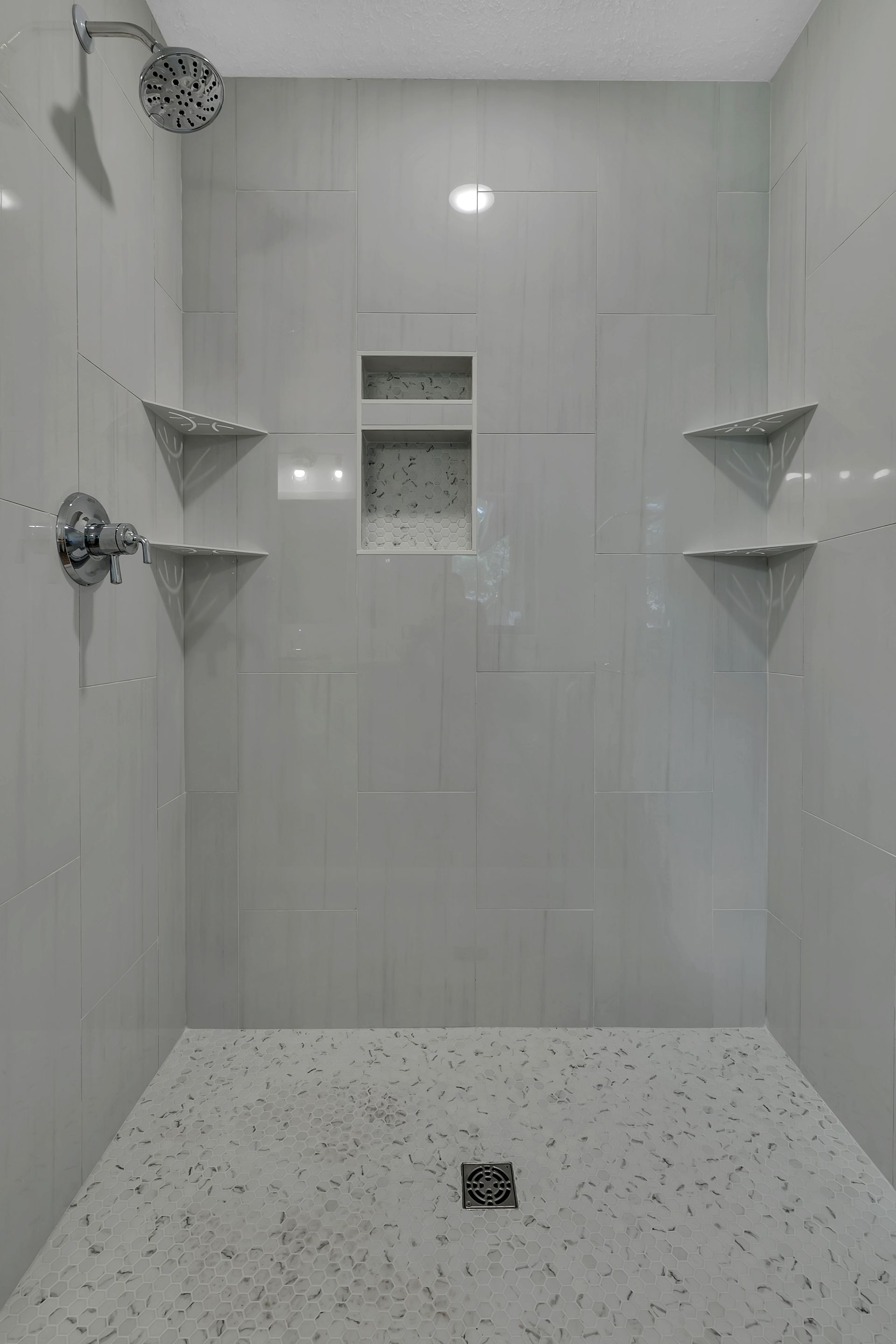 A shower with two shower heads and shelves in a bathroom.