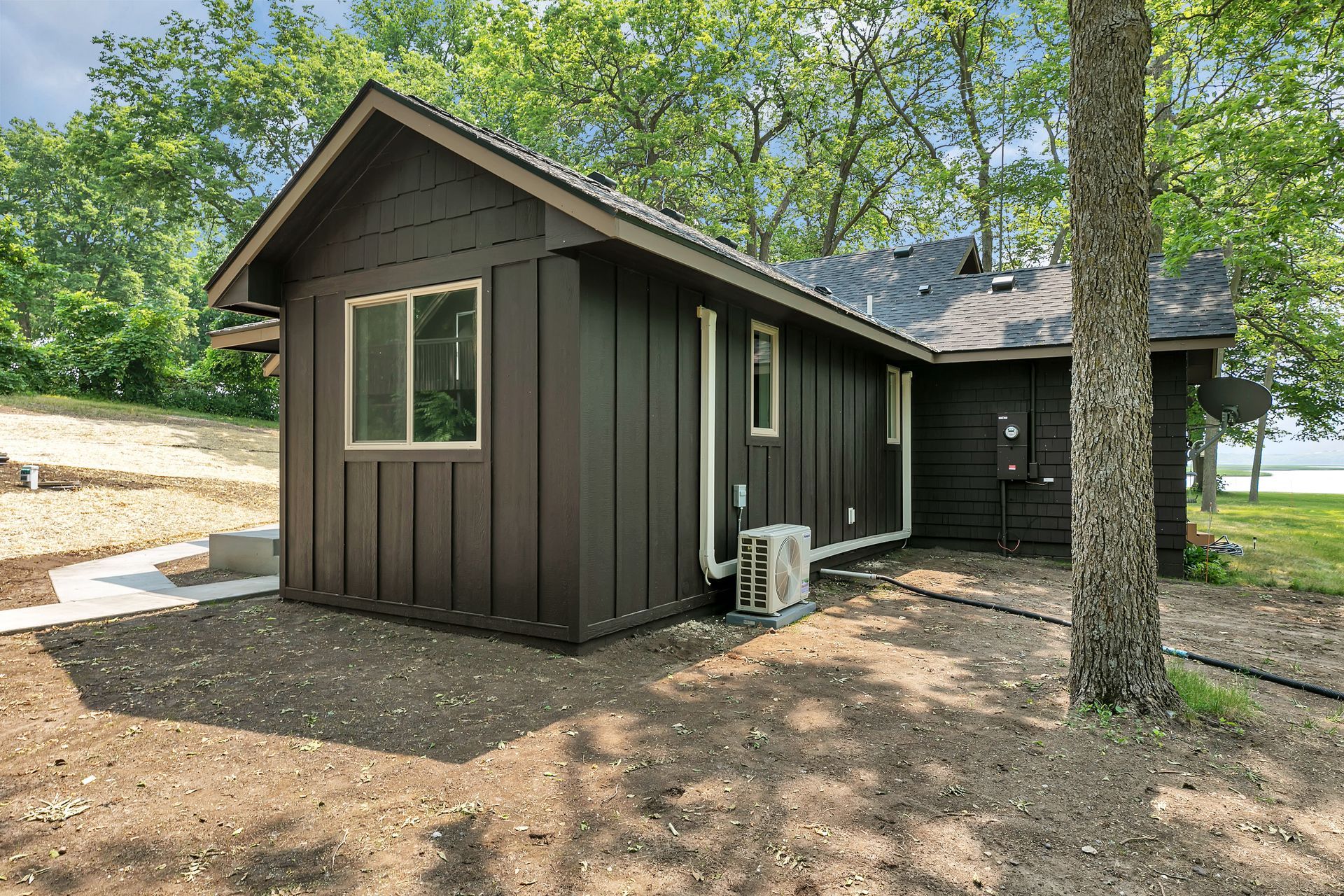 A small black house with a lot of windows is sitting next to a tree.