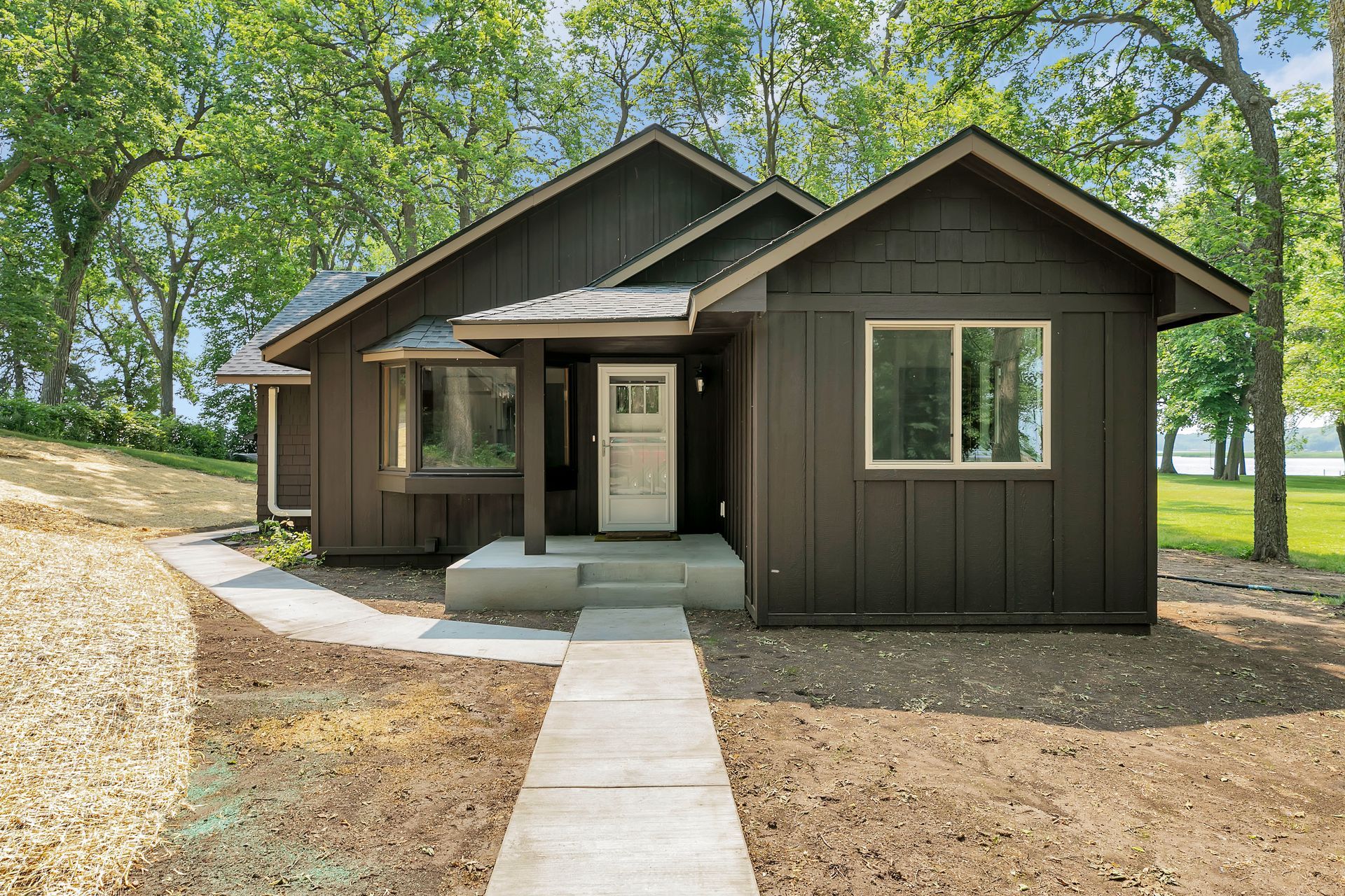 A small house with a walkway leading to it is surrounded by trees.