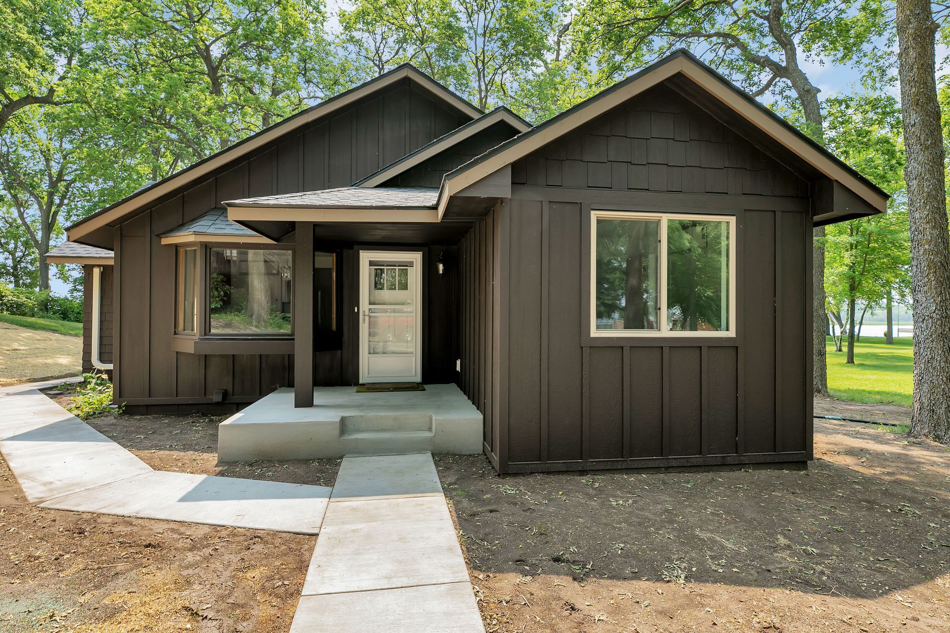 A small brown house with a walkway leading to it is surrounded by trees.