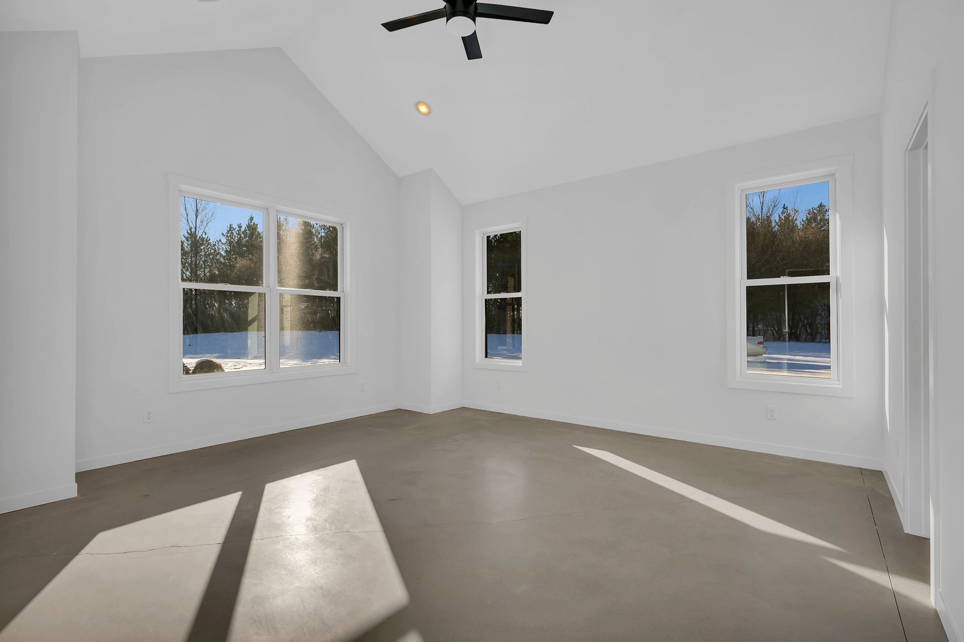 An empty room with a ceiling fan and three windows.