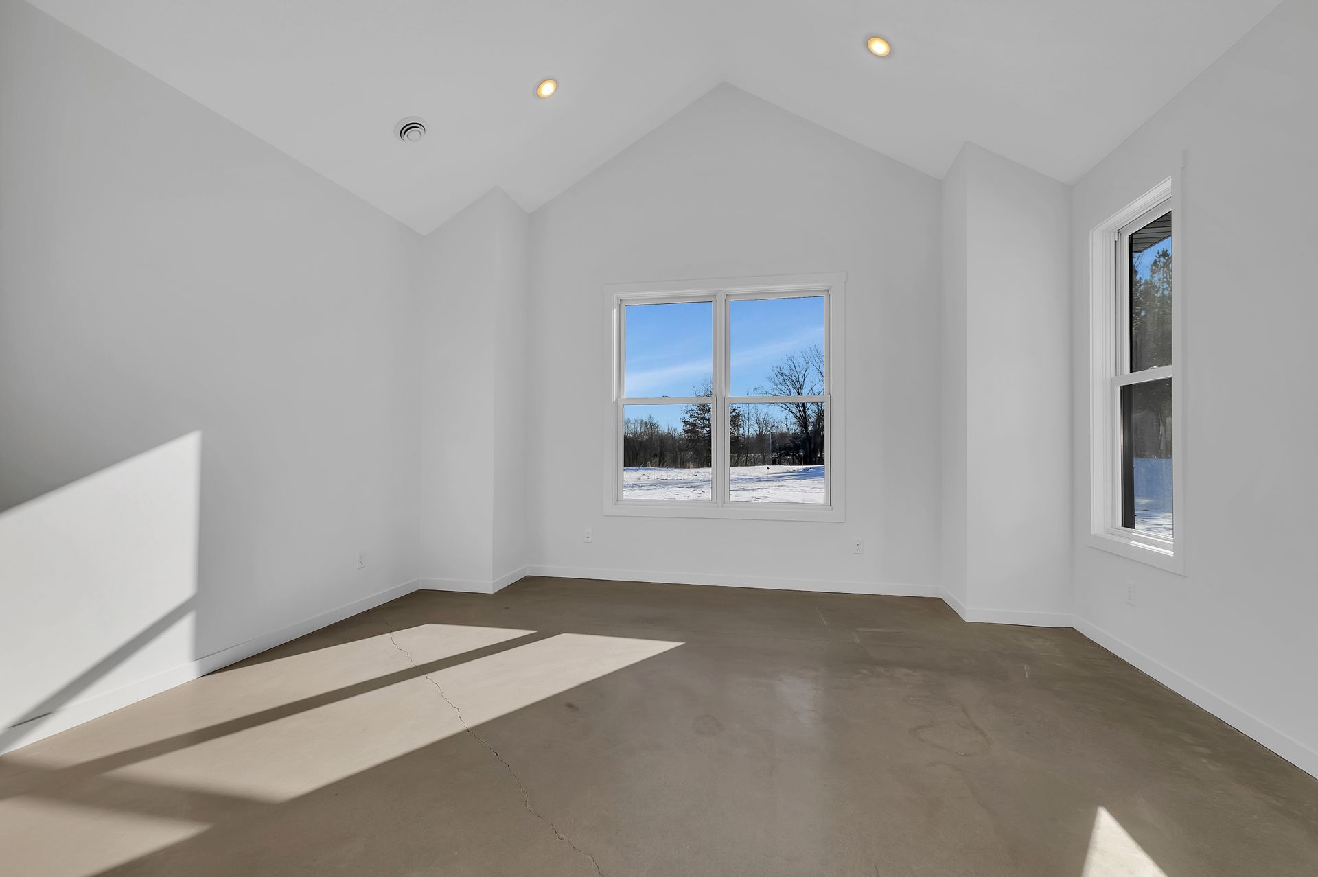 An empty room with a vaulted ceiling and two windows.