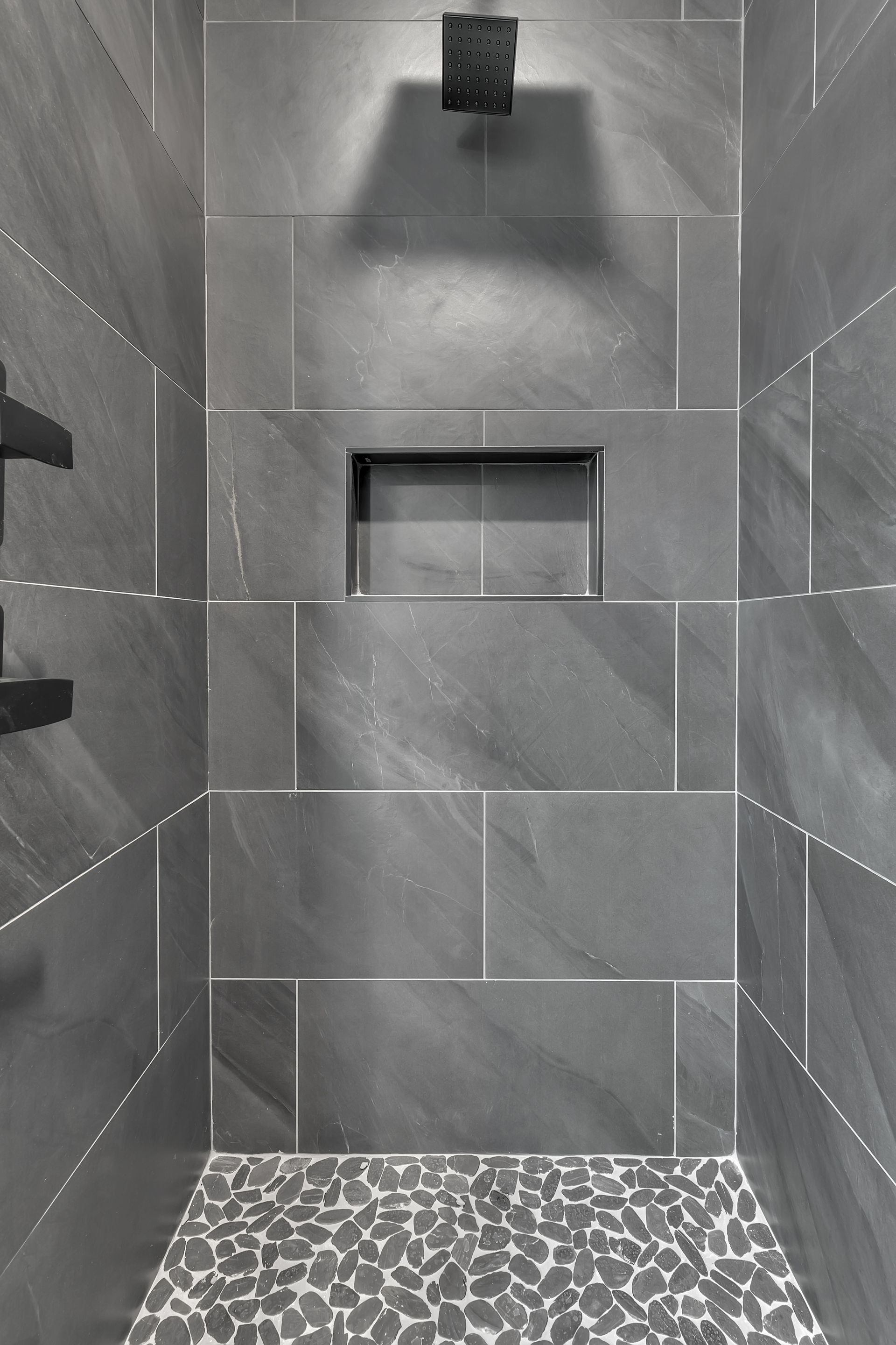 A black and white photo of a shower with gray tiles and a mosaic floor.