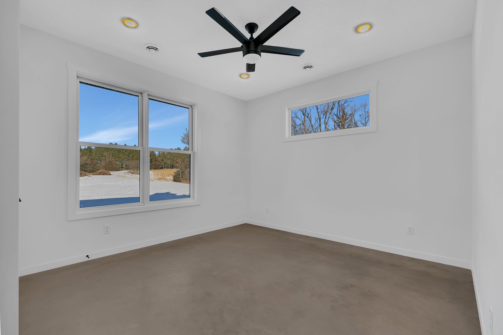 An empty bedroom with a ceiling fan and two windows.