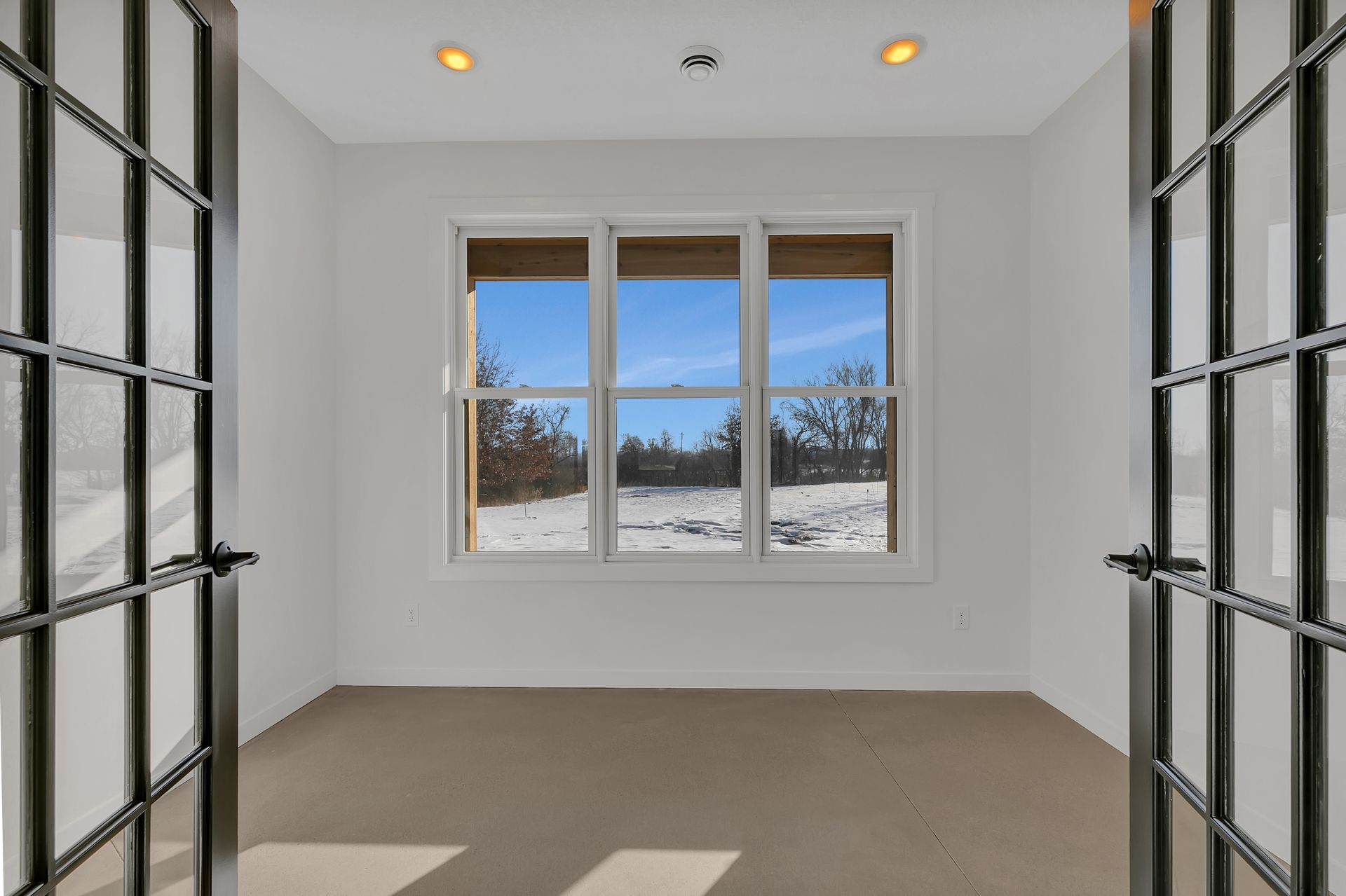 An empty room with two windows and a view of a snowy field.