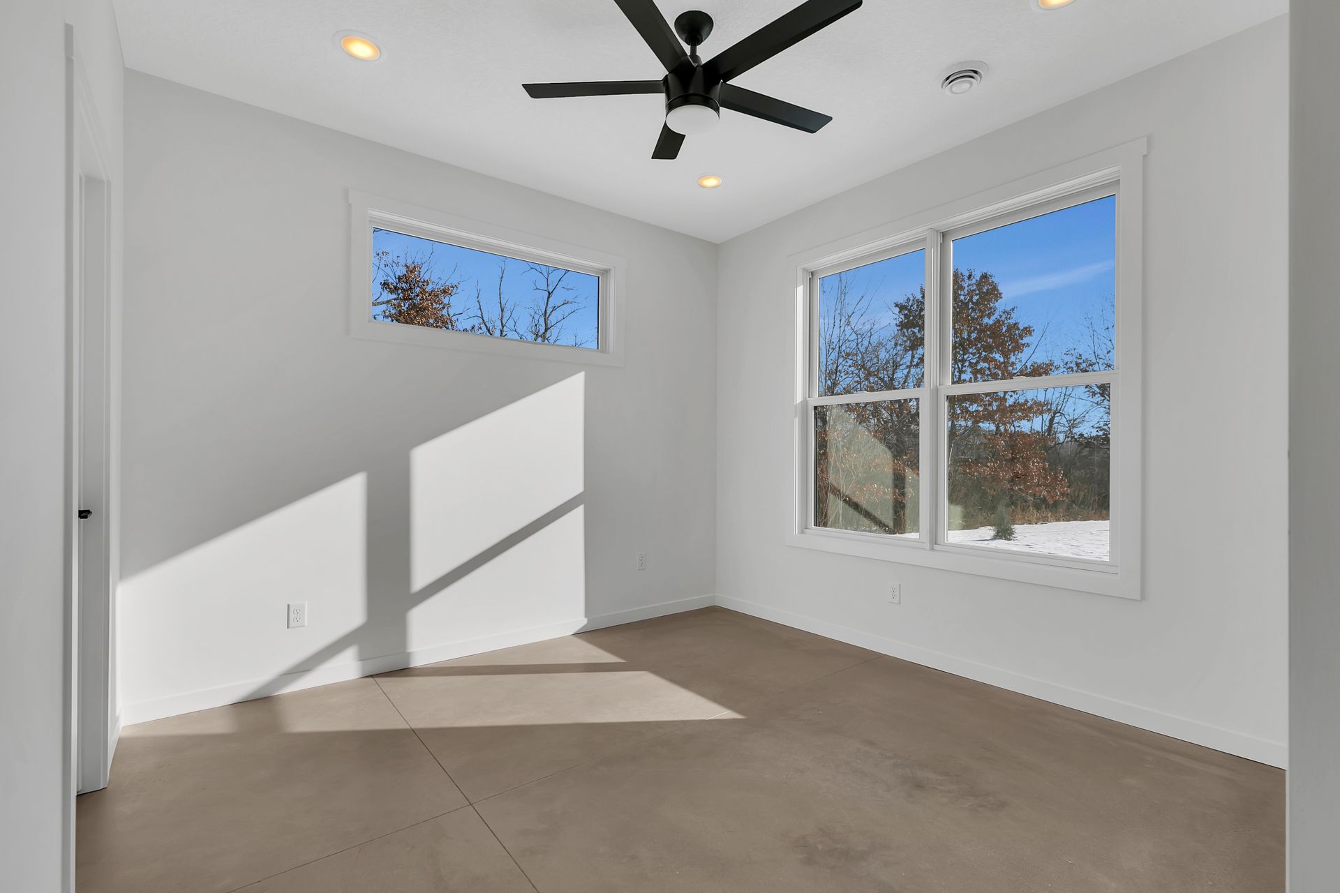 An empty bedroom with a ceiling fan and two windows.
