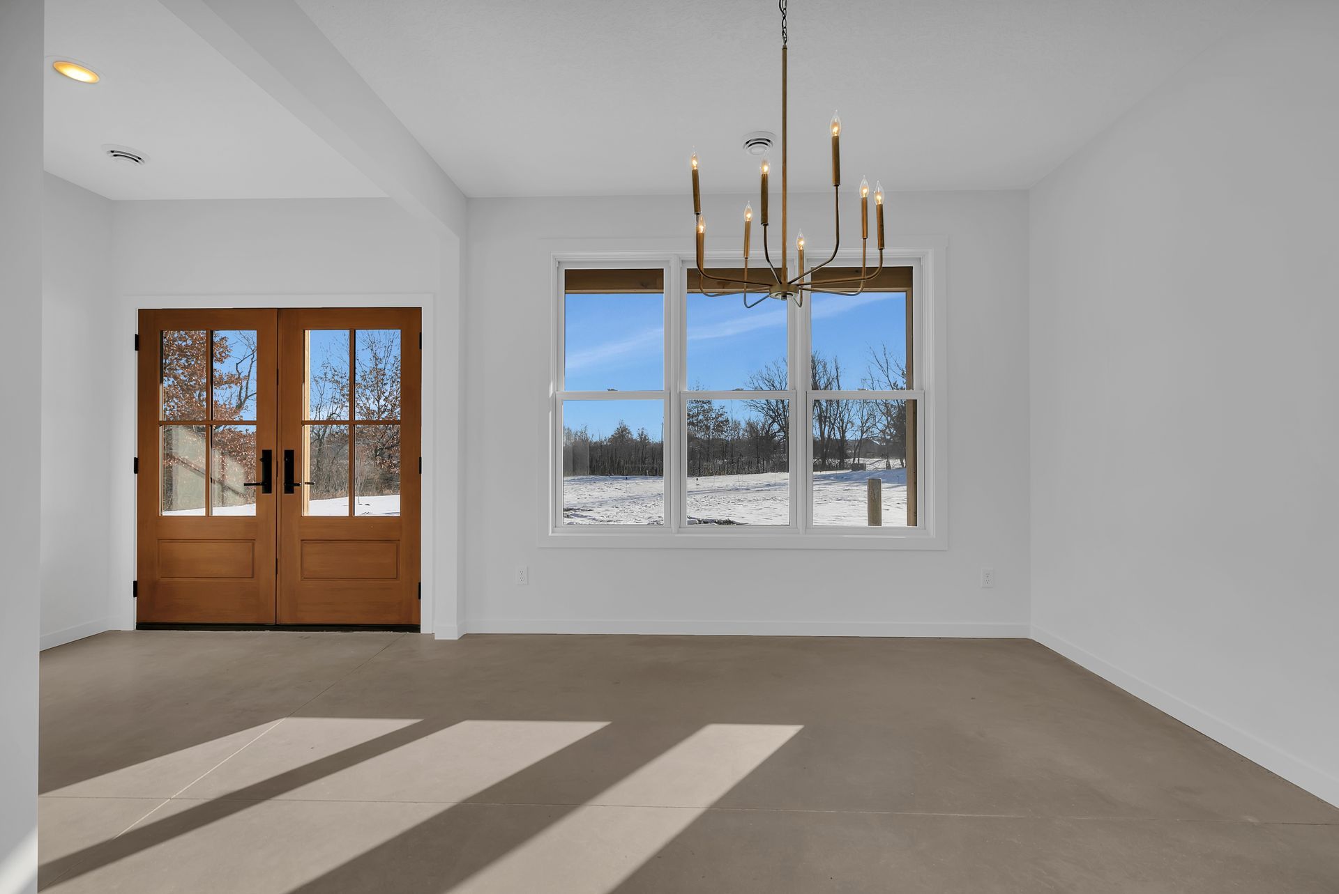An empty living room with a chandelier and two windows.