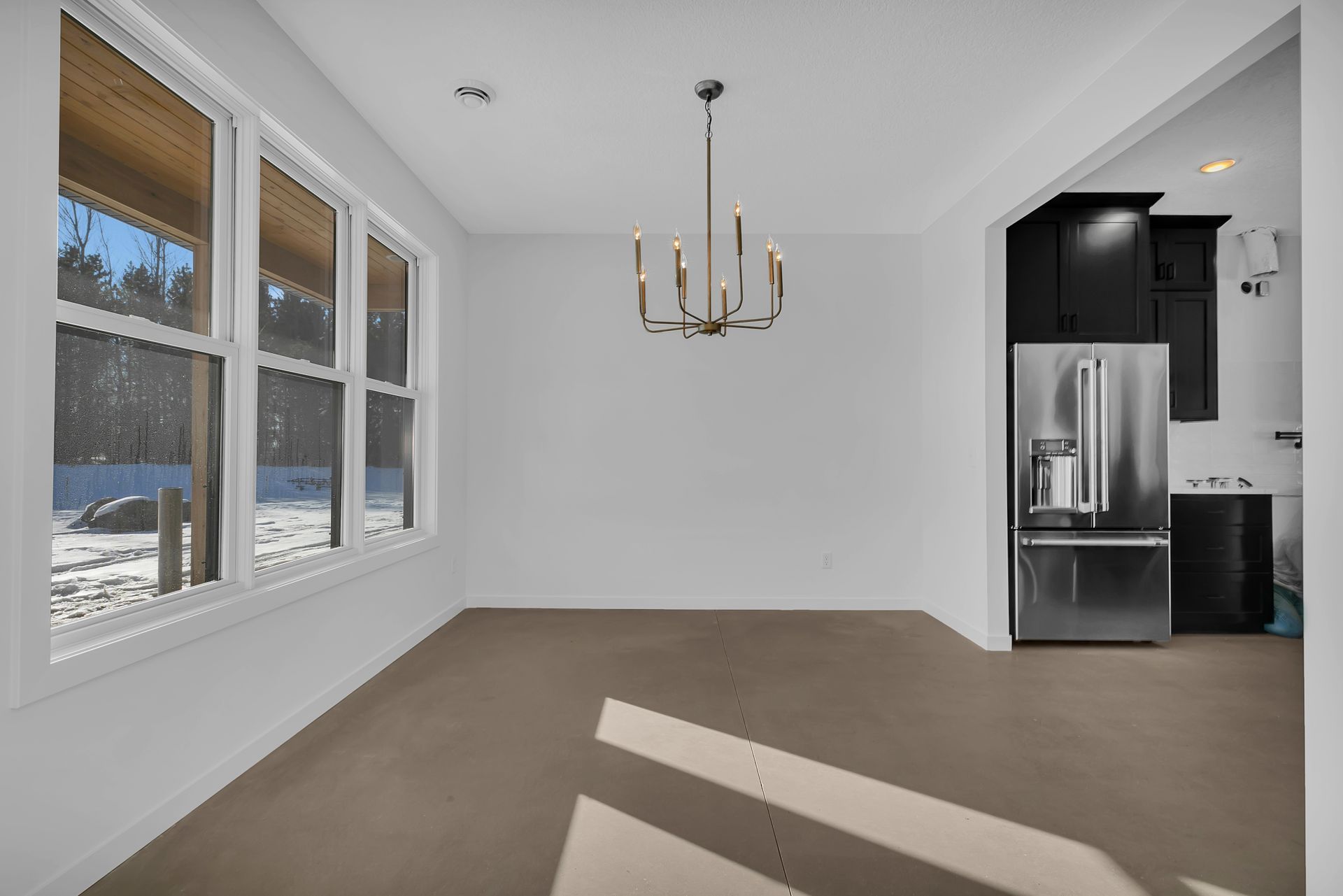 An empty dining room with a chandelier and a refrigerator.