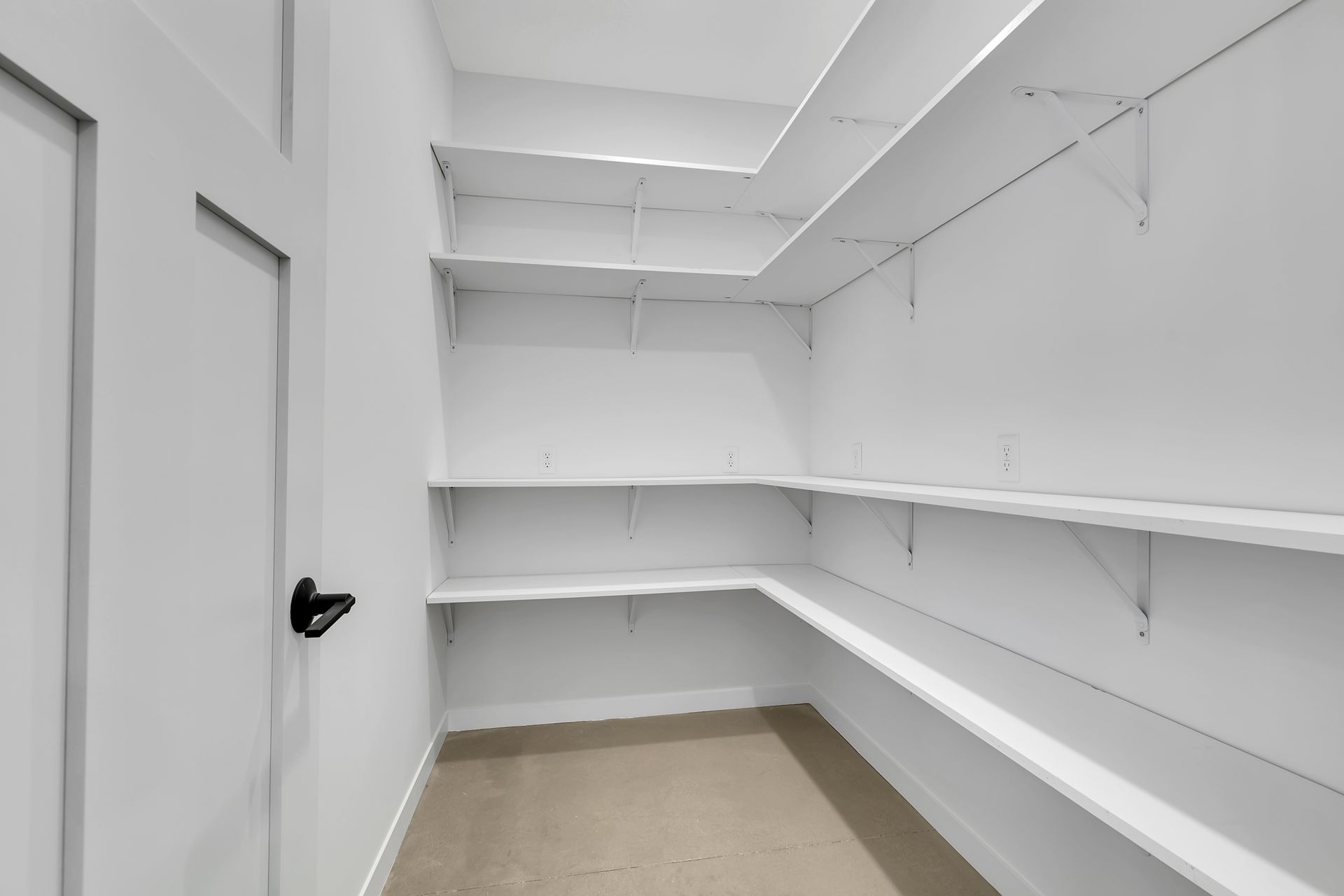 An empty walk in closet with white shelves and a door.
