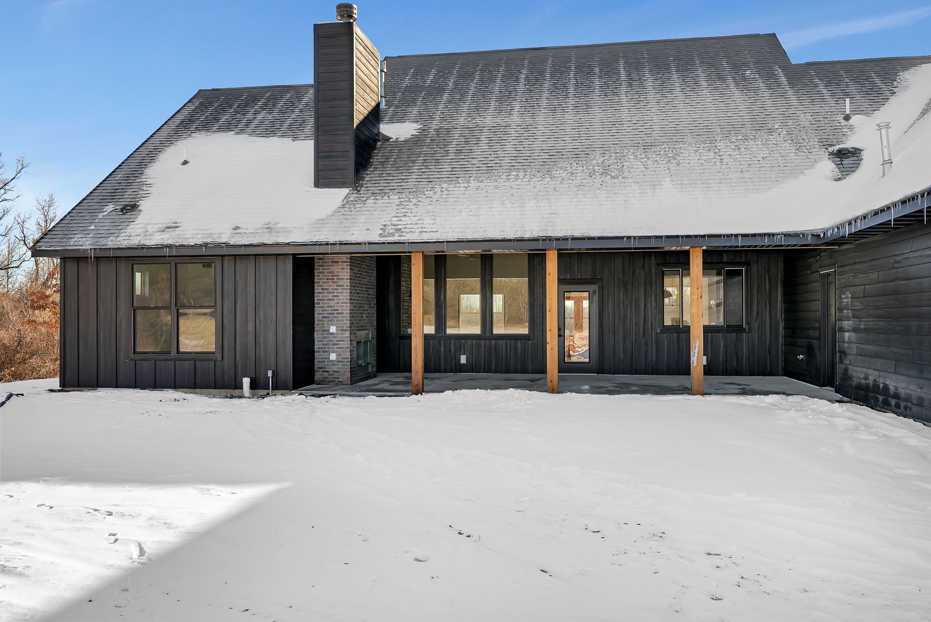 A black house with a porch in the snow.
