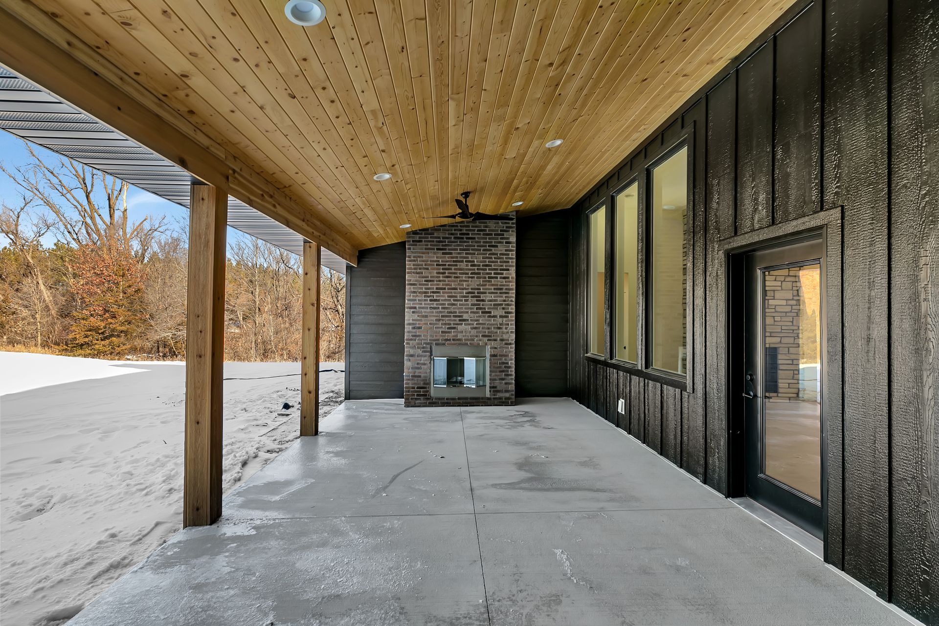 A large covered patio with a fireplace and a wooden ceiling.