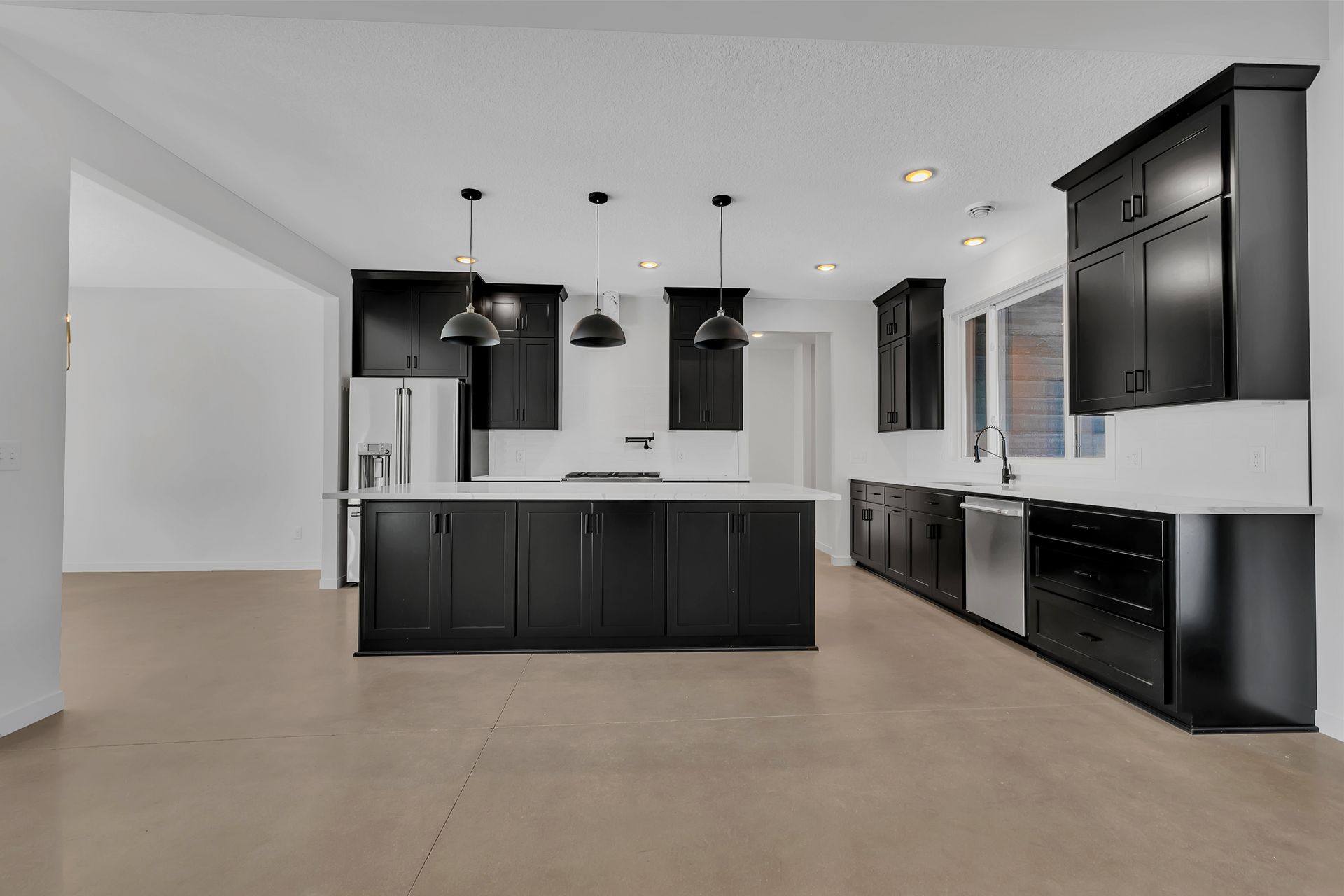 An empty kitchen with black cabinets and stainless steel appliances.