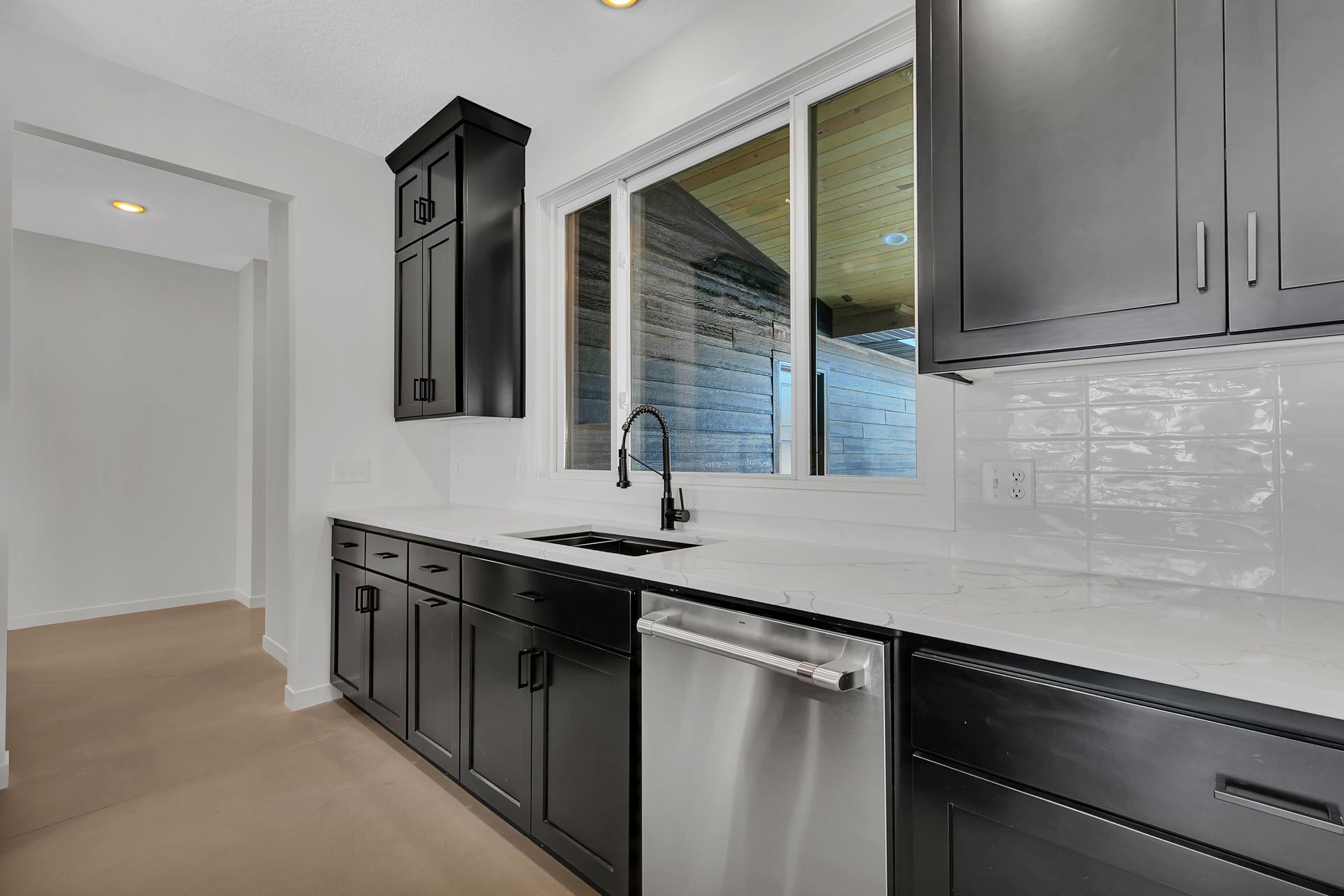 A kitchen with black cabinets , stainless steel appliances , and a large window.