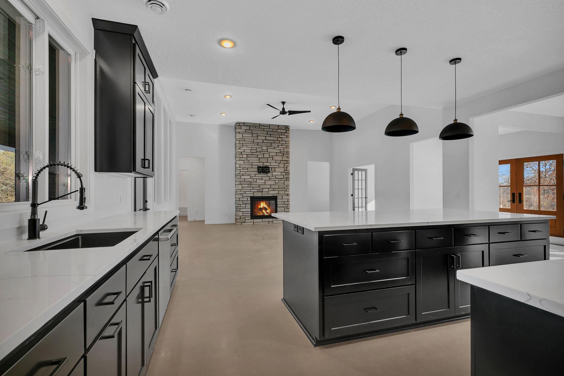 A kitchen with black cabinets , a large island , a sink , and a fireplace.
