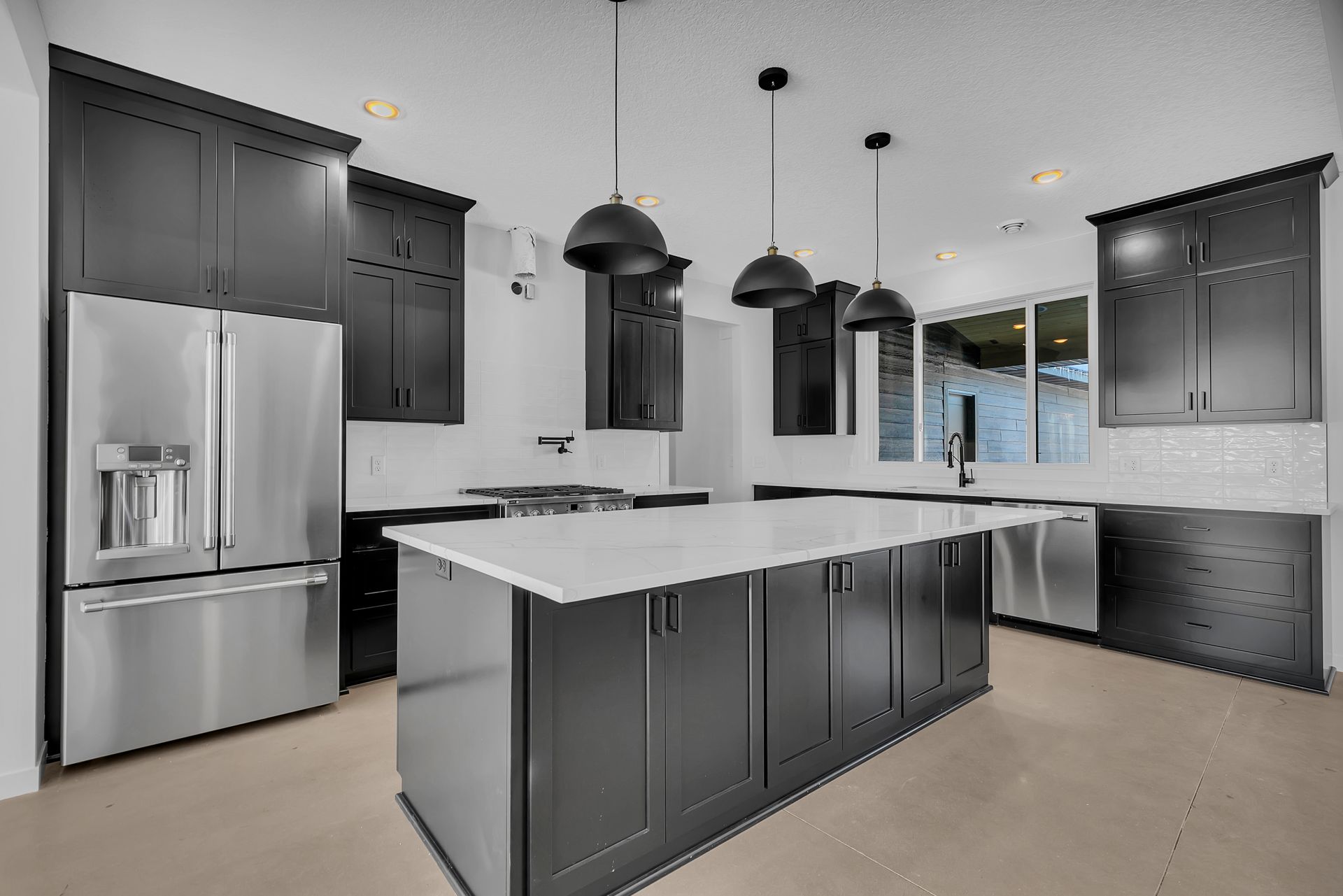 A kitchen with black cabinets , stainless steel appliances , and a large island.