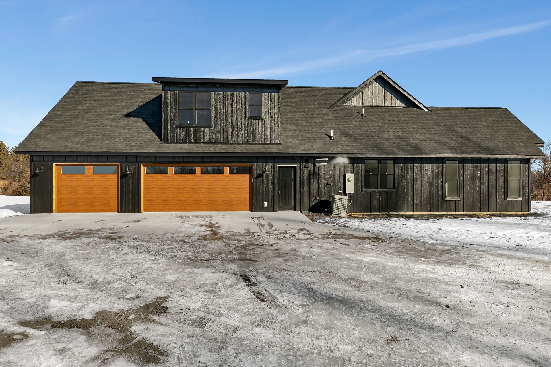 A large house with three garage doors is sitting in the middle of a snowy field.